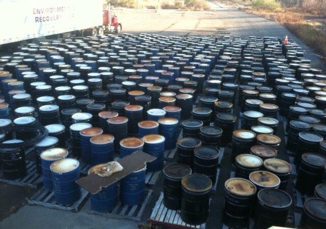 Large number of industrial barrels arranged outdoors at a waste recovery or materials handling facility.
