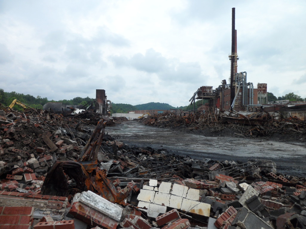 Large industrial demolition site with piles of brick and metal debris surrounding a partially dismantled factory.