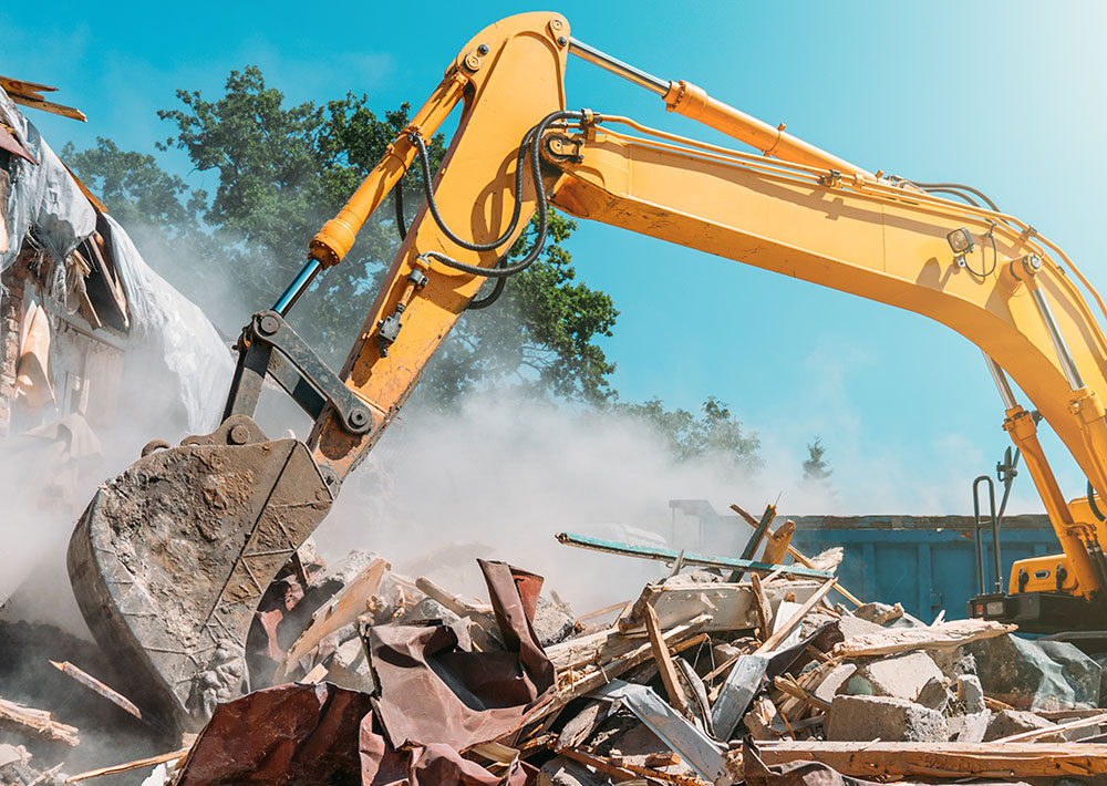 Excavator demolishing a building and clearing construction debris at a job site.