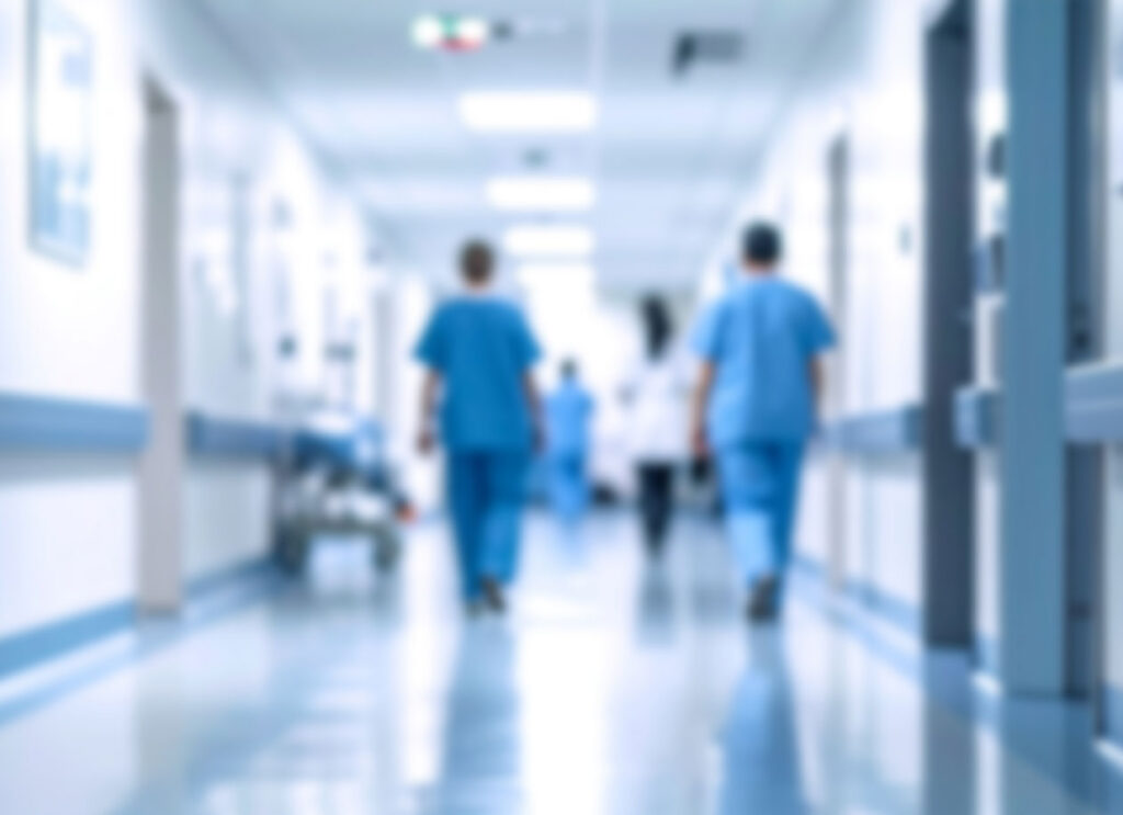Blurry hospital hallway with medical staff in scrubs walking down a bright corridor.